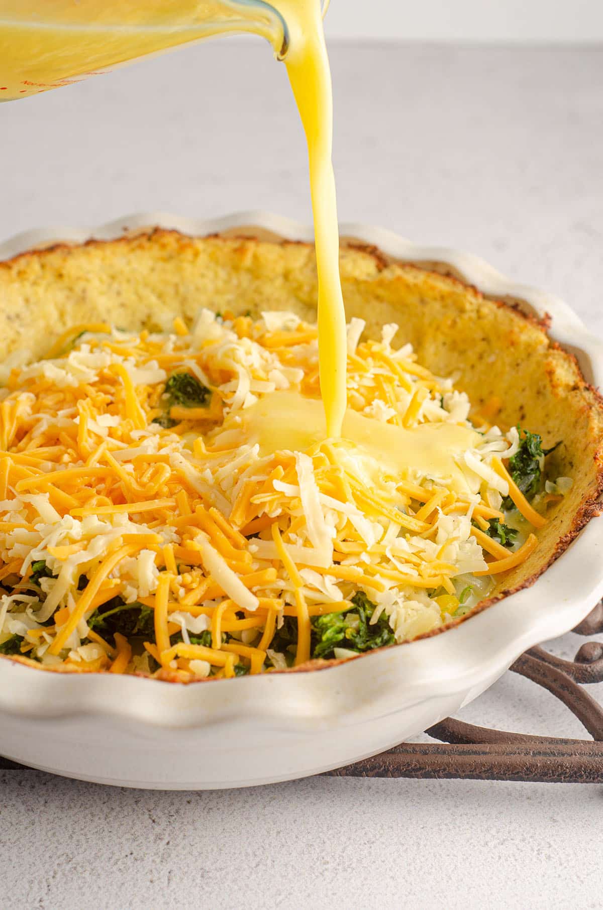 pouring egg mixture onto quiche filling in a pie plate