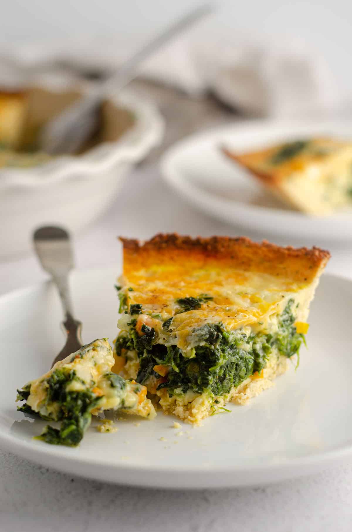 slice of cheesy vegetable quiche with cauliflower crust sitting on a plate