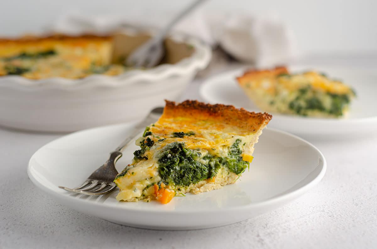 slice of cheesy vegetable quiche with cauliflower crust sitting on a plate