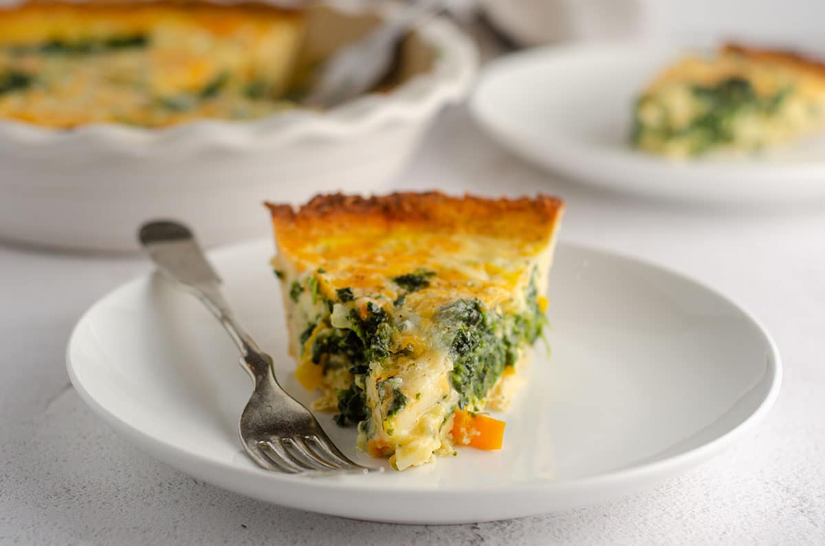 slice of cheesy vegetable quiche with cauliflower crust sitting on a plate