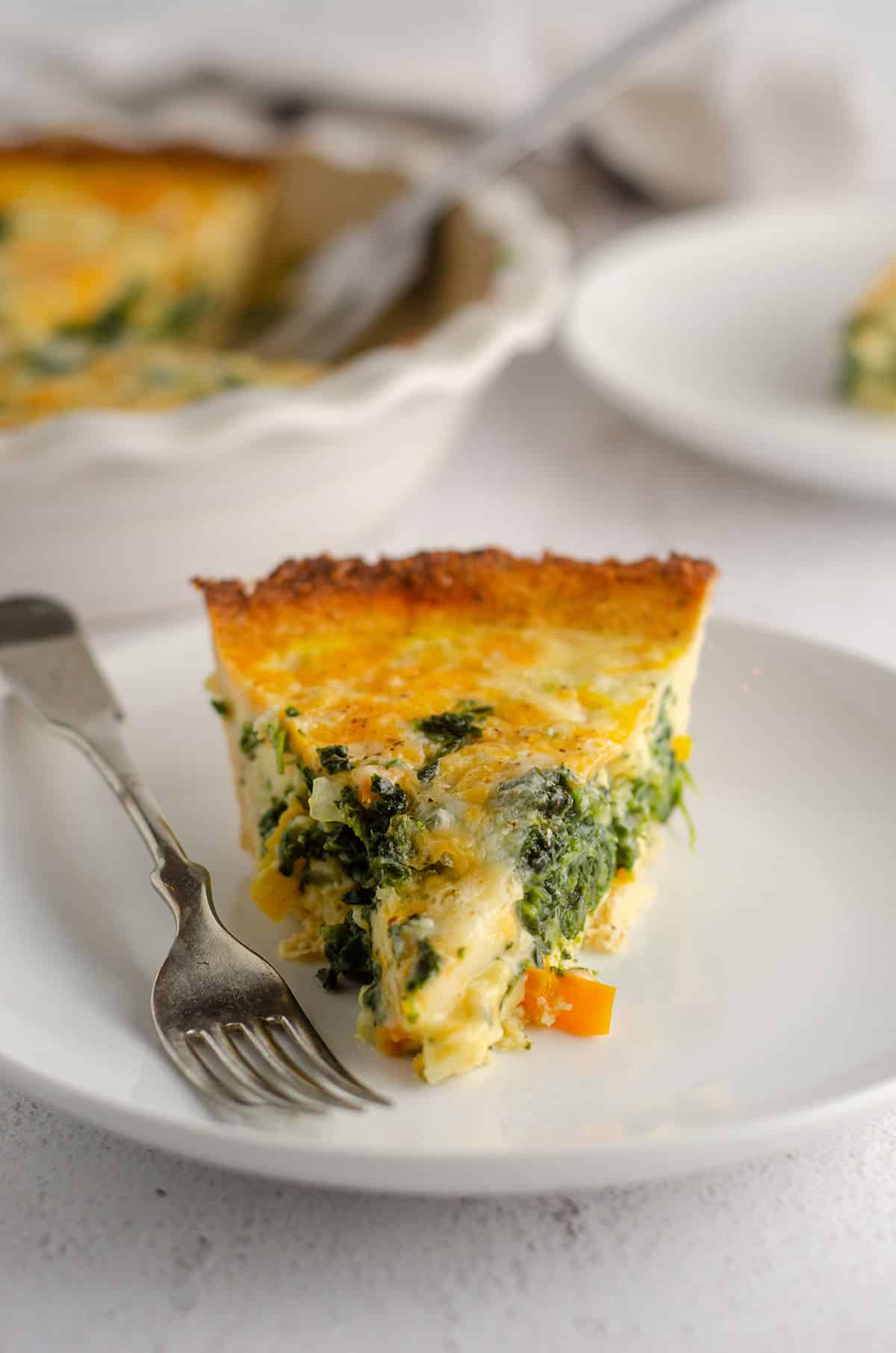 slice of cheesy vegetable quiche with cauliflower crust sitting on a plate