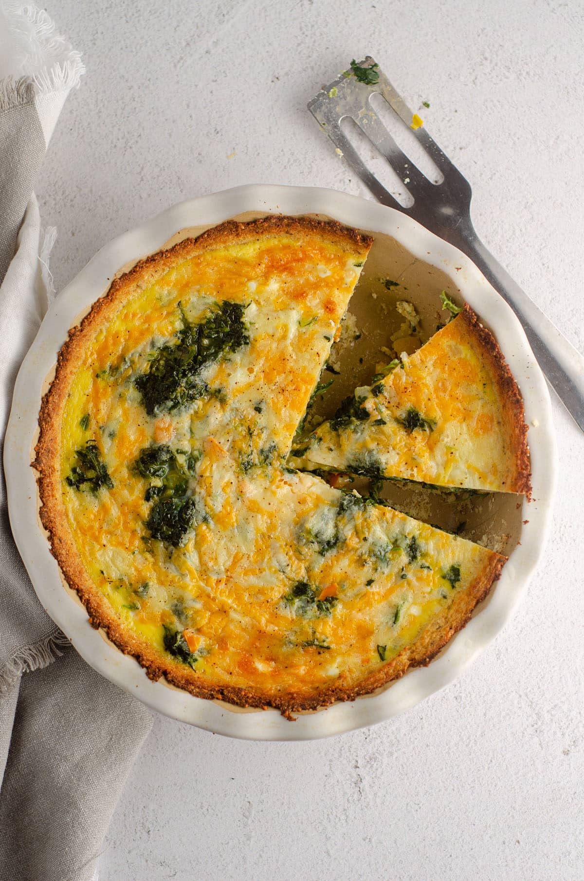 aerial photo of cheesy vegetable quiche with cauliflower crust in a pie plate with a slice cut out