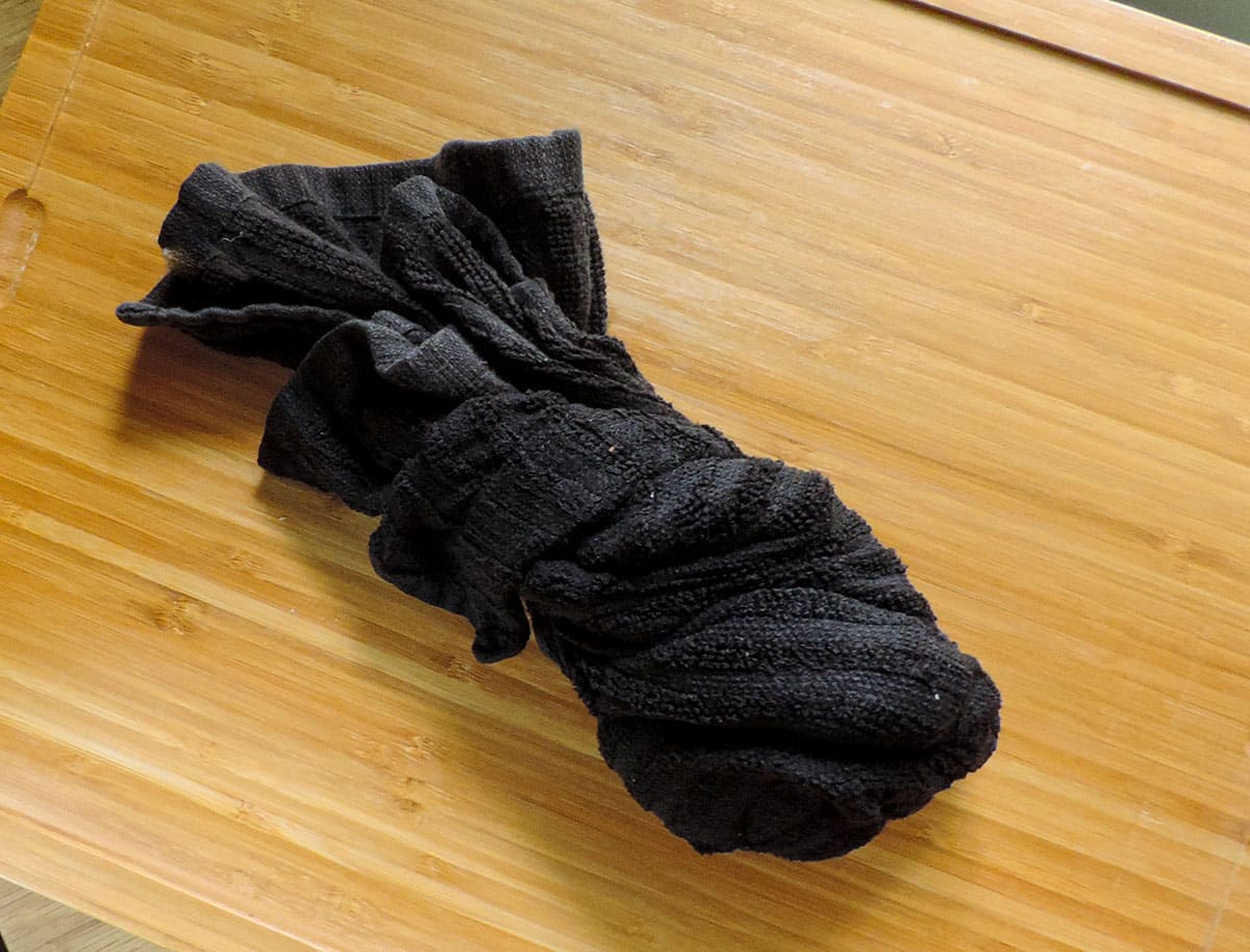 black kitchen towel being used to squeeze moisture out of cooked cauliflower