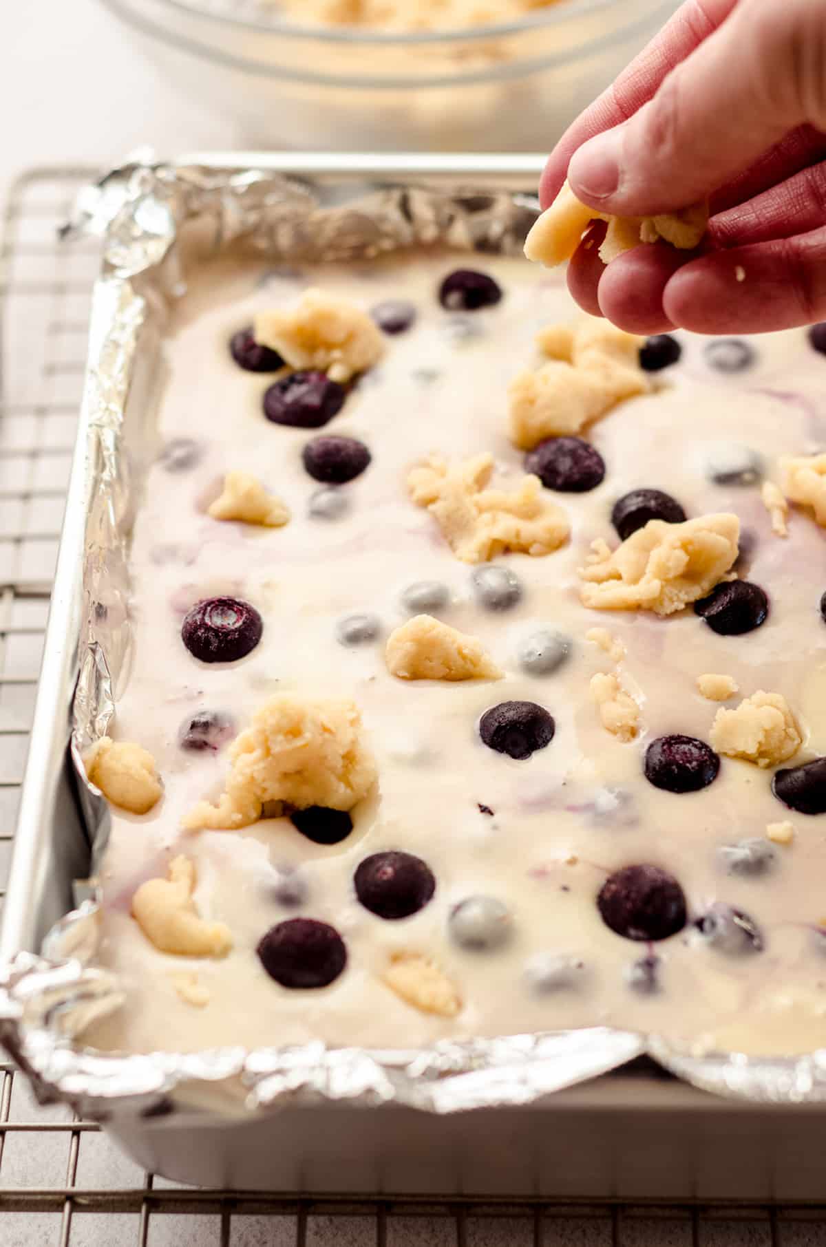 hand dropping crumbles of shortbread crust onto blueberry lemon bars