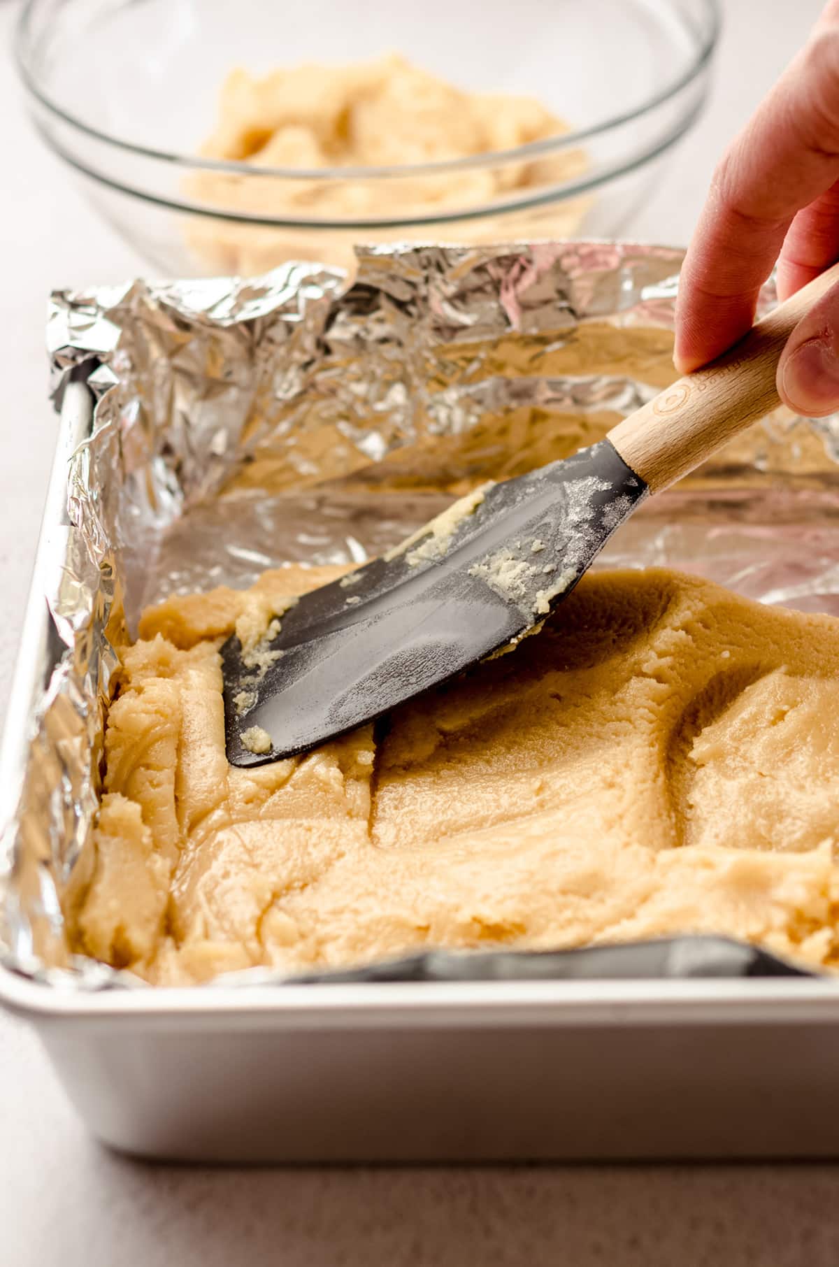 spatula pressing shortbread crust into a square baking pan