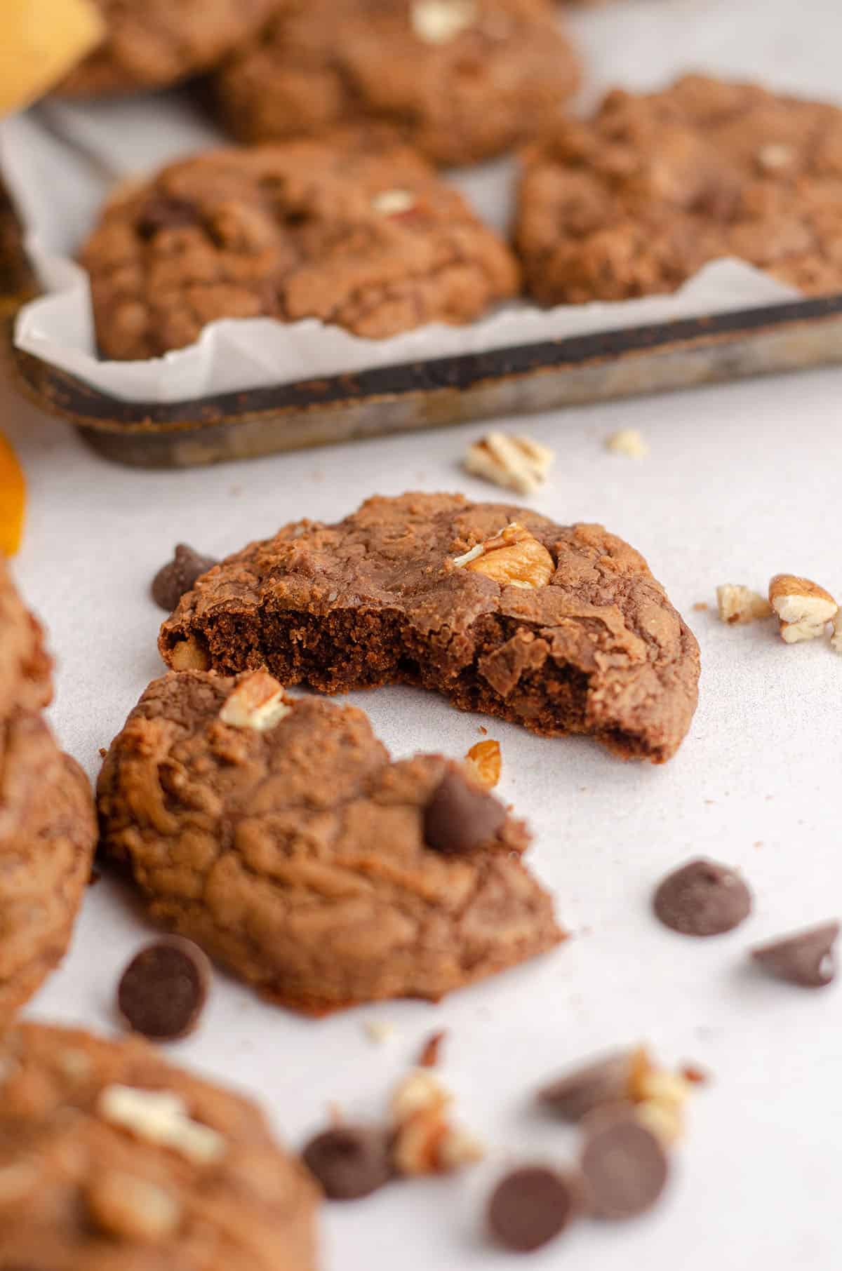 a brownie cookie broken in half with chocolate chips and nuts scattered around it