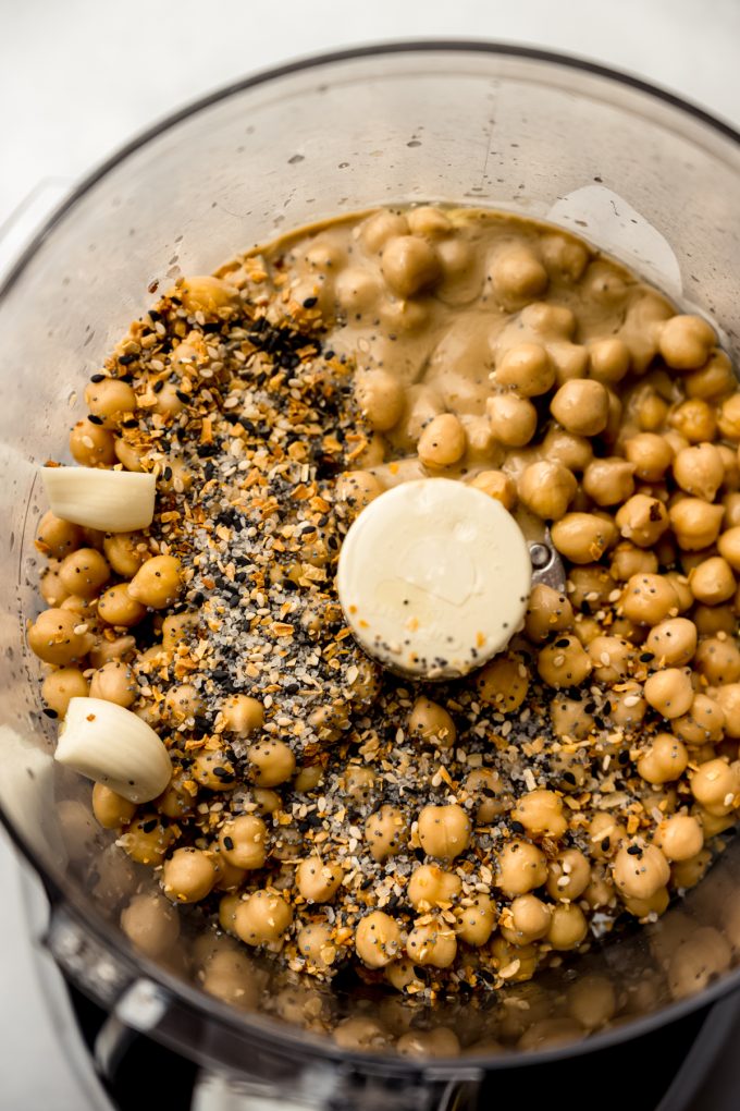Aerial photo of the ingredients to make everything bagel hummus in the drum of a food processor.