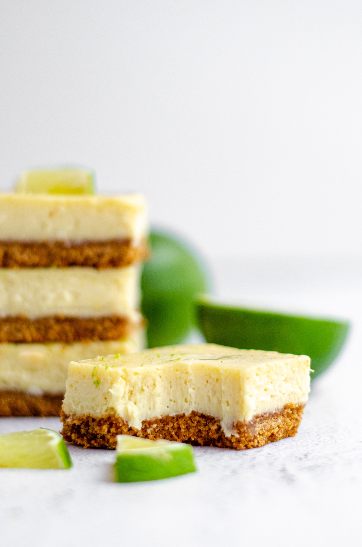 a key lime pie bar in the foreground with a bite taken out of it and a stack of key lime pie bars in the background