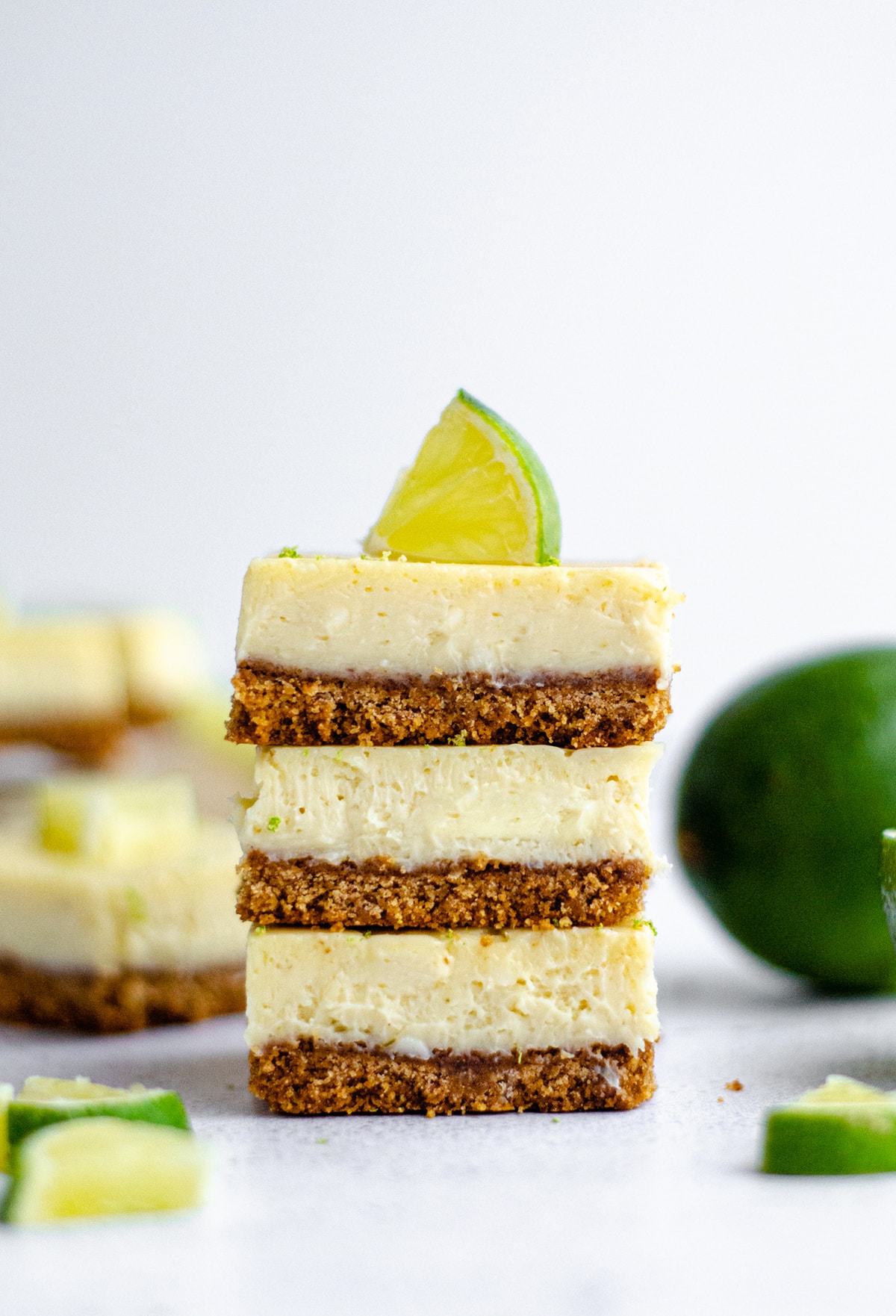 stack of key lime pie bars with slices of lime scattered around and on top of the stack