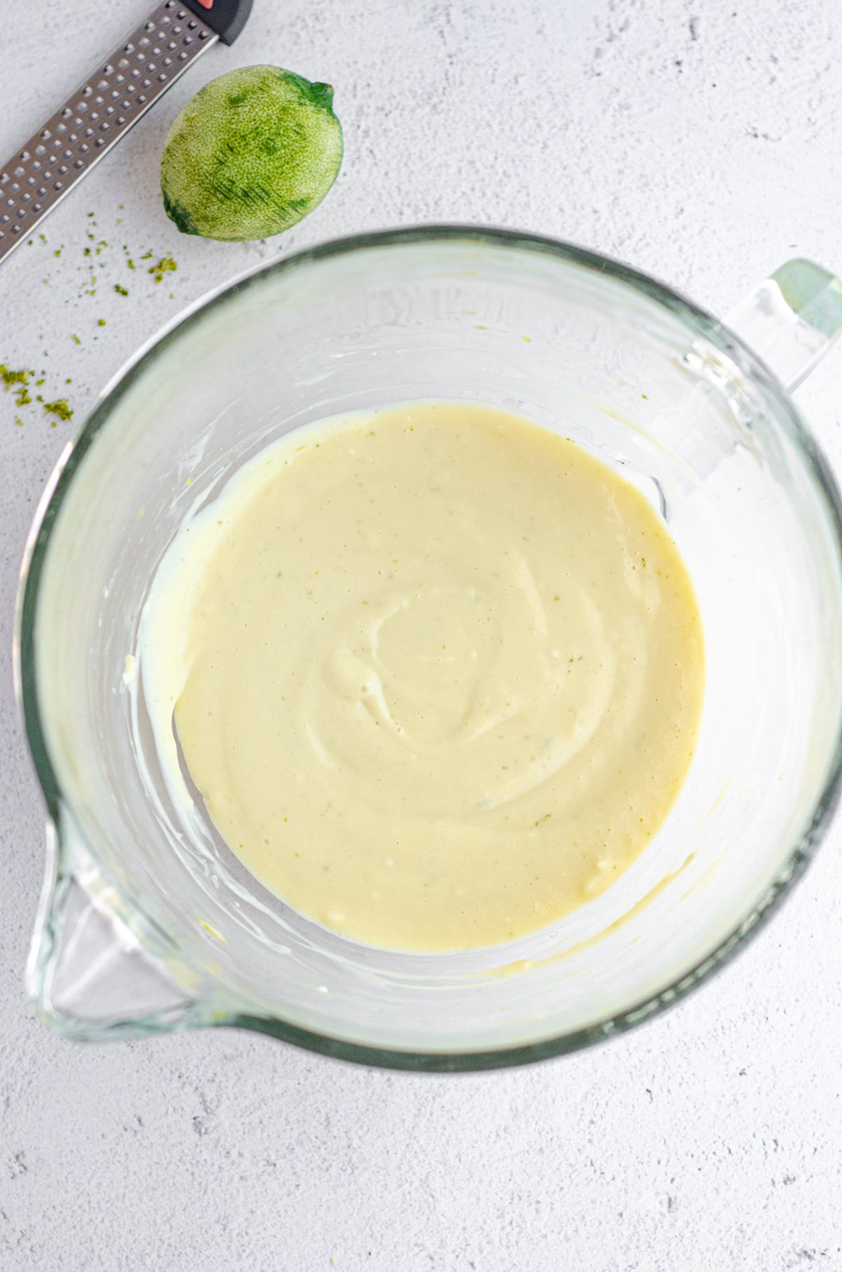 aerial photo of key lime pie bar batter in a glass mixing bowl and a zested lime off to the side