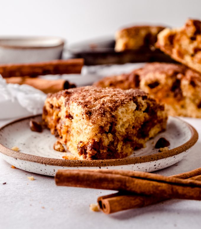 A cinnamon scone on a plate with cinnamon sticks in the foreground and background.