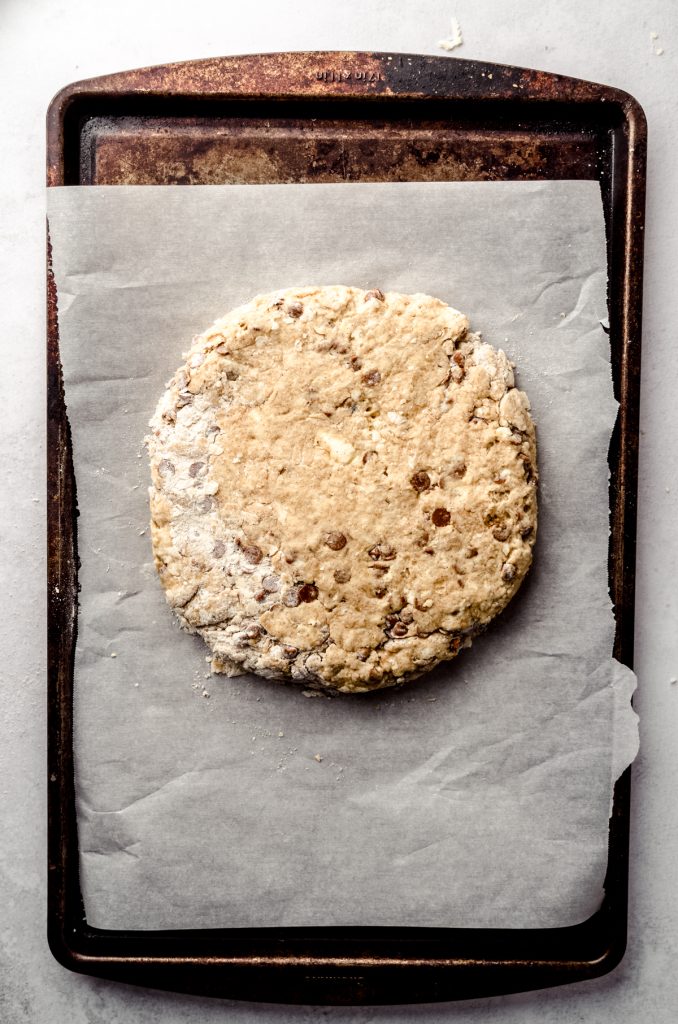 A disc of cinnamon scone dough on a piece of parchment.