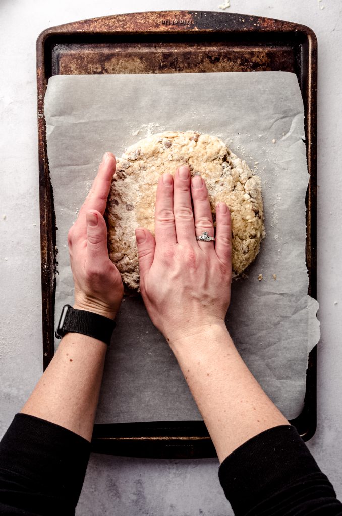 Aerial photo of someone pressing scone dough into a disc with their hands.