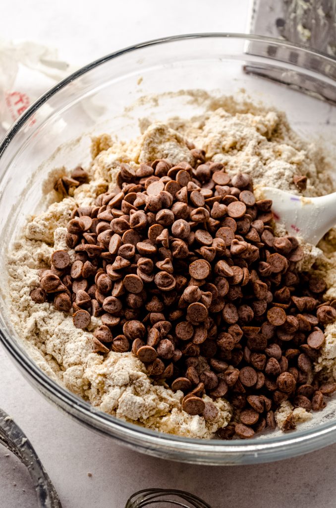 A bowl of scone dough with cinnamon chips and a spatula in it.
