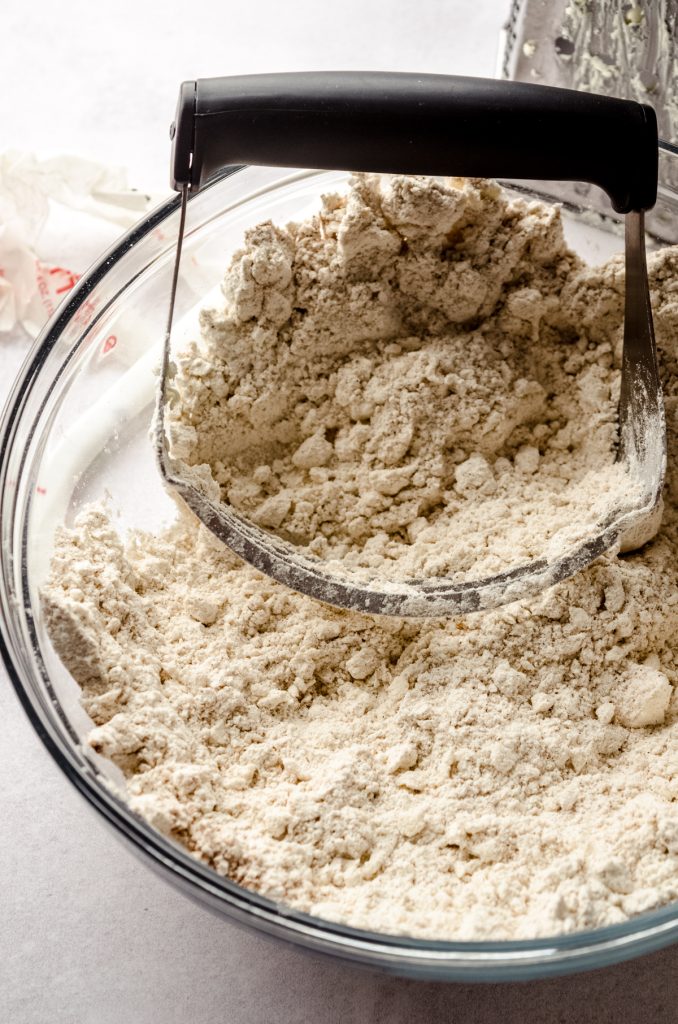 A pastry cutter in a bowl of dry ingredients with butter cut into it to make scones.