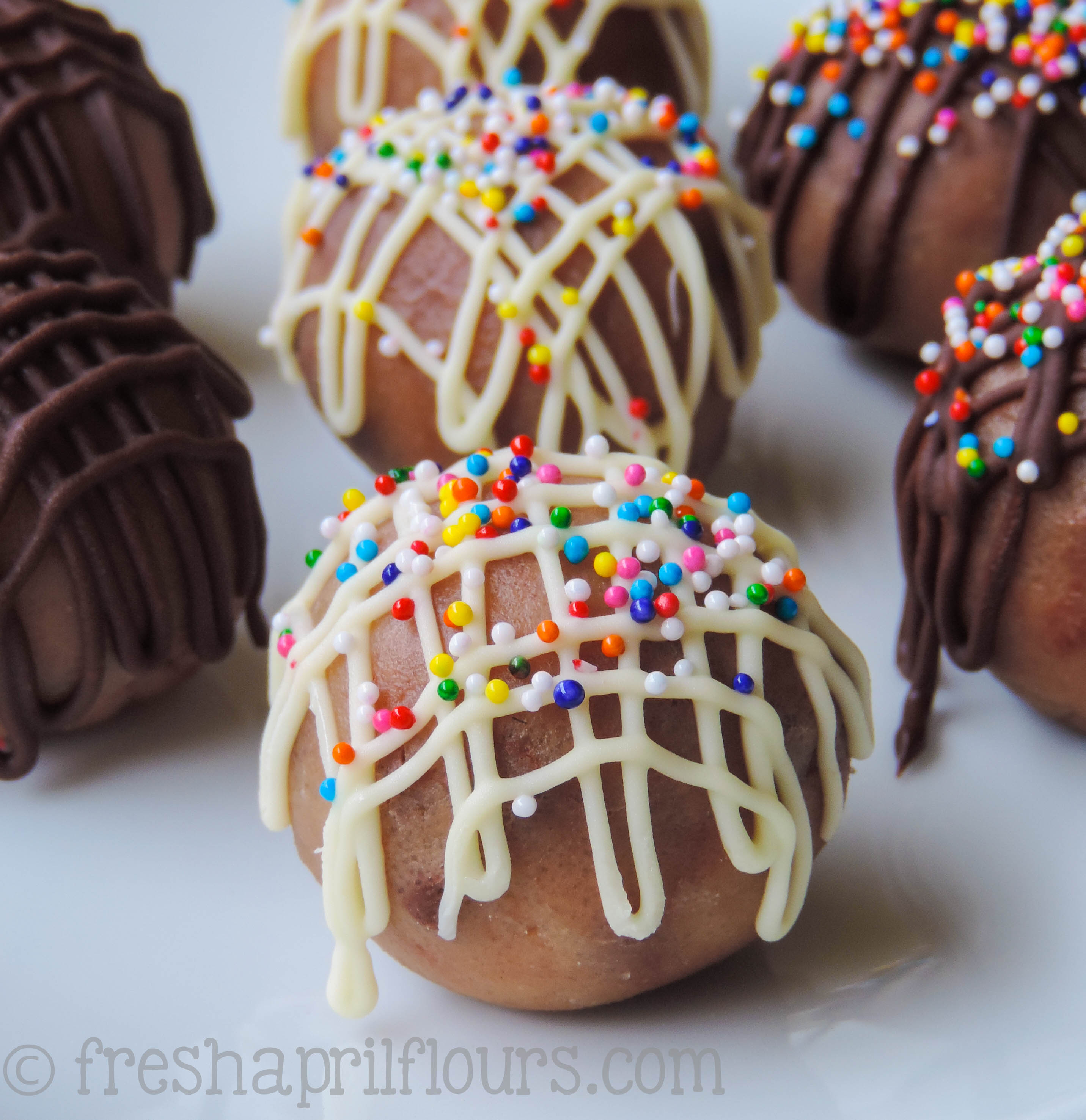 a cookie dough bite with white chocolate and sprinkles drizzled on it