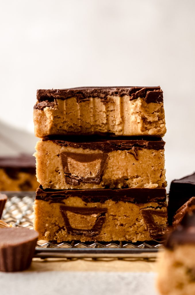 Three peanut butter bars stacked on top of each other and the one on the top has a bite taken out of it.