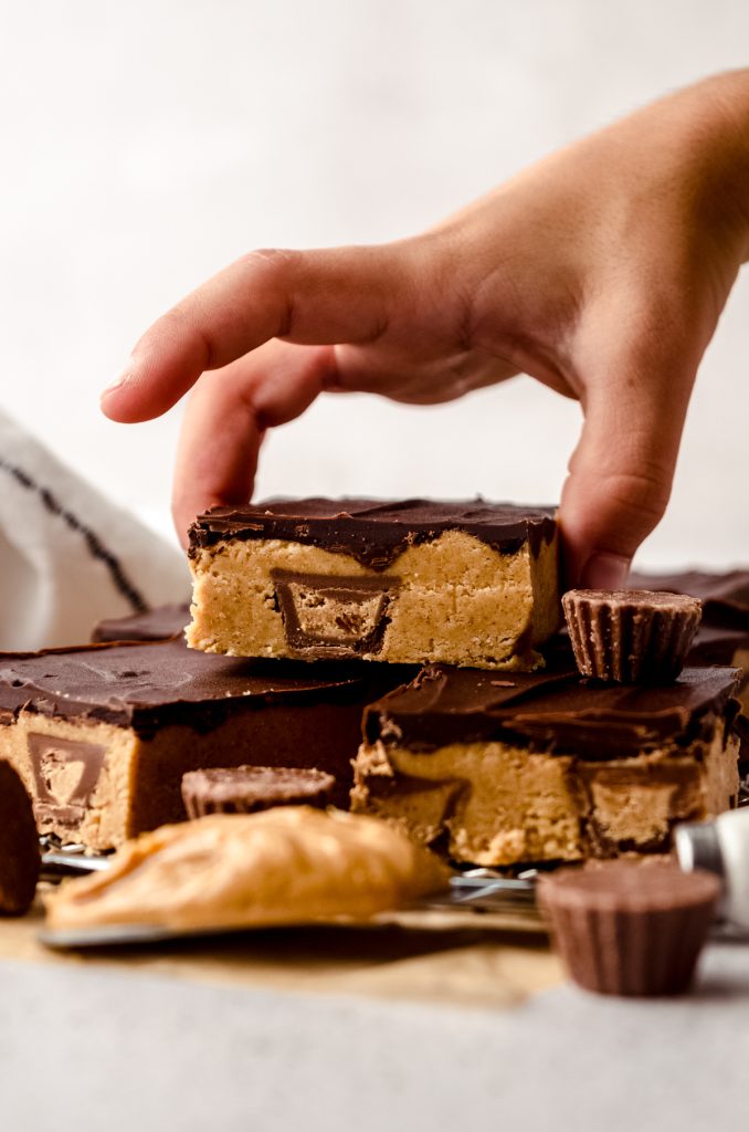 A stack of peanut butter bars on a surface and a child's hand is grabbing the one on the top.