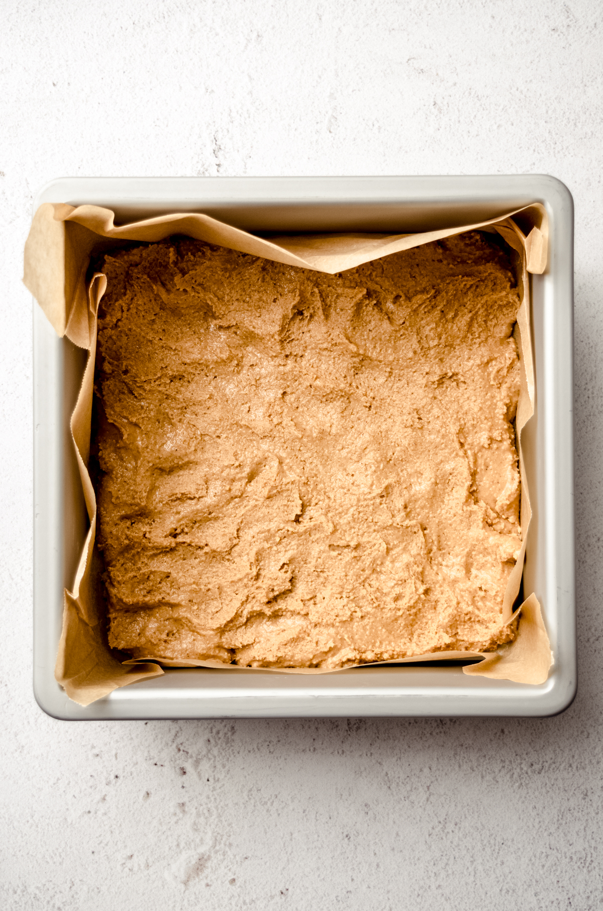 Aerial photo of the bottom layer of peanut butter filling pressed into a baking pan to make peanut butter bars.