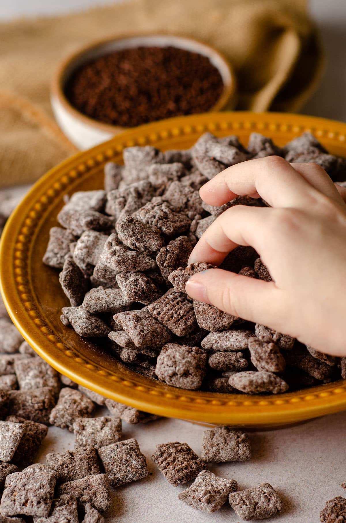 toddler hand grabbing brownie batter puppy chow from a bowl