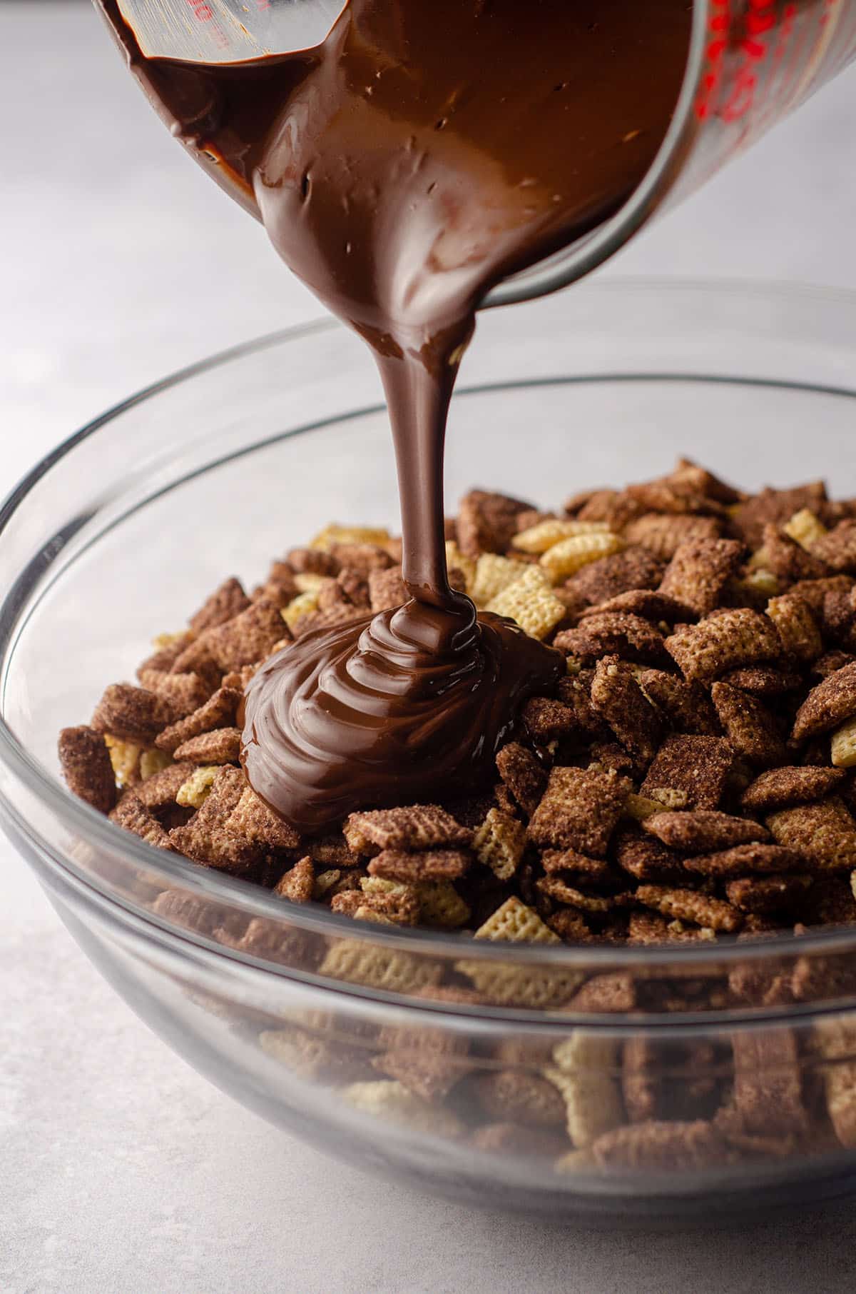 melted chocolate being poured onto chocolate chex cereal to make brownie batter puppy chow