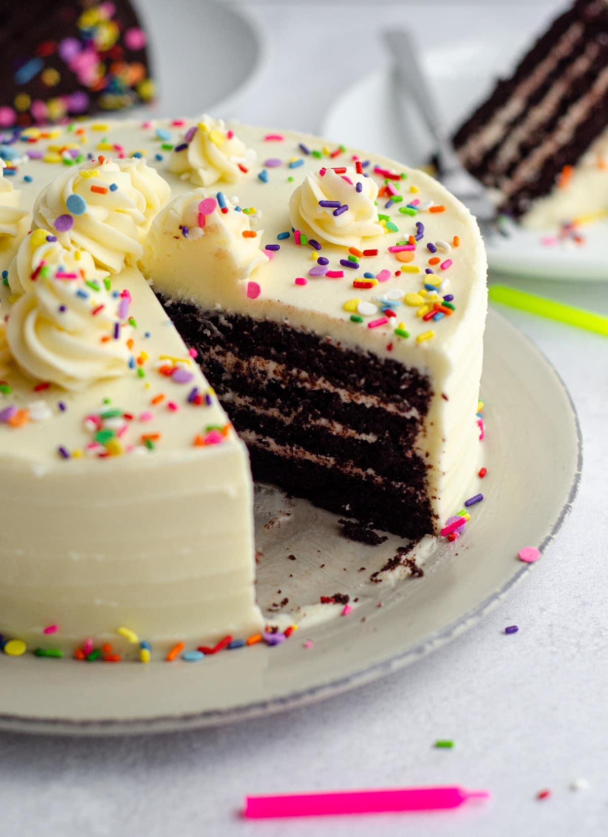 chocolate layer cake with vanilla buttercream and rainbow sprinkles on a plate with a slice taken out of it