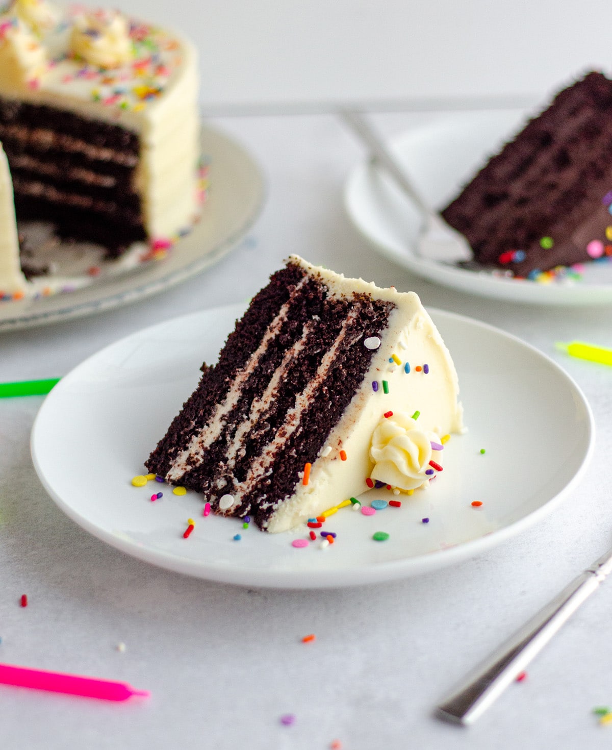chocolate layer cake with vanilla buttercream and rainbow sprinkles on a white plate