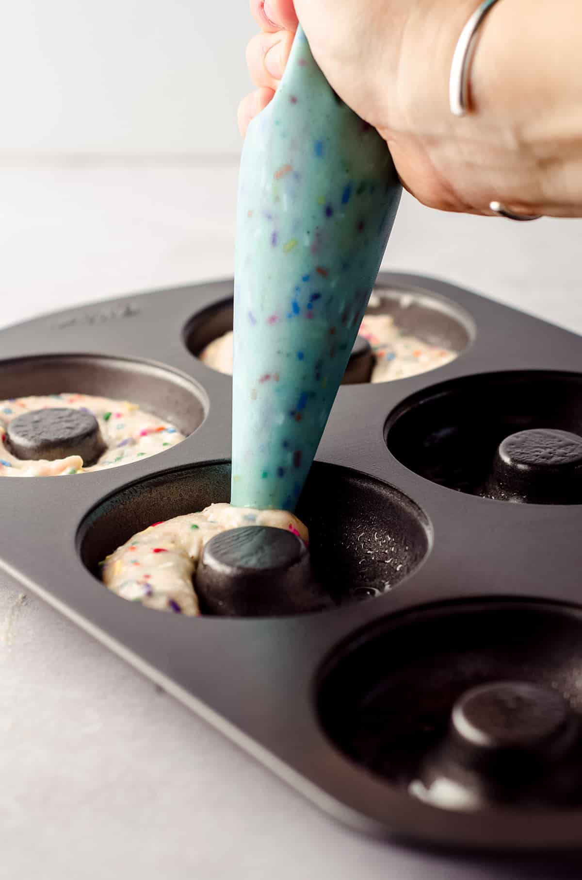 filling a donut pan with funfetti donut batter with a piping bag