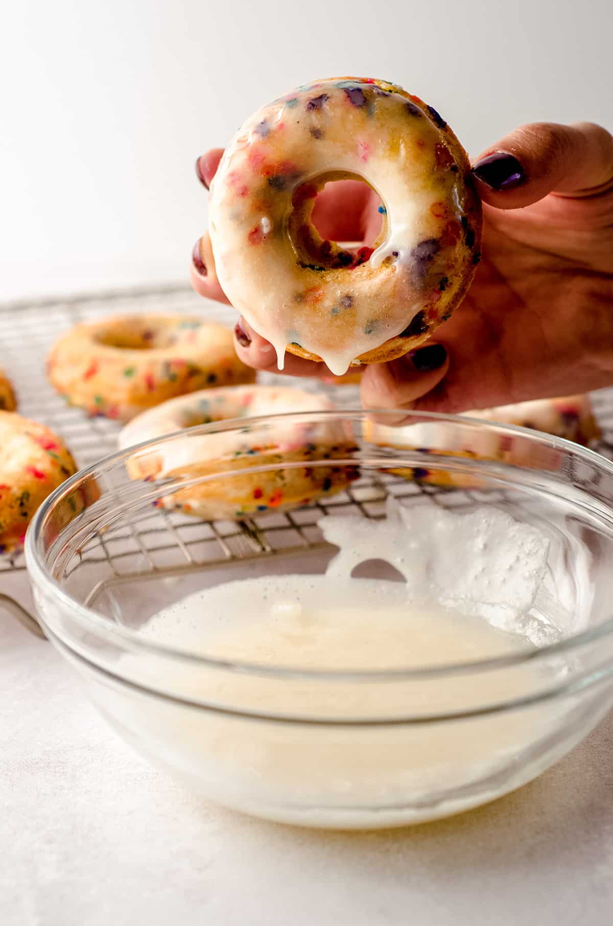hand holding a funfetti donut after dipping it into glaze