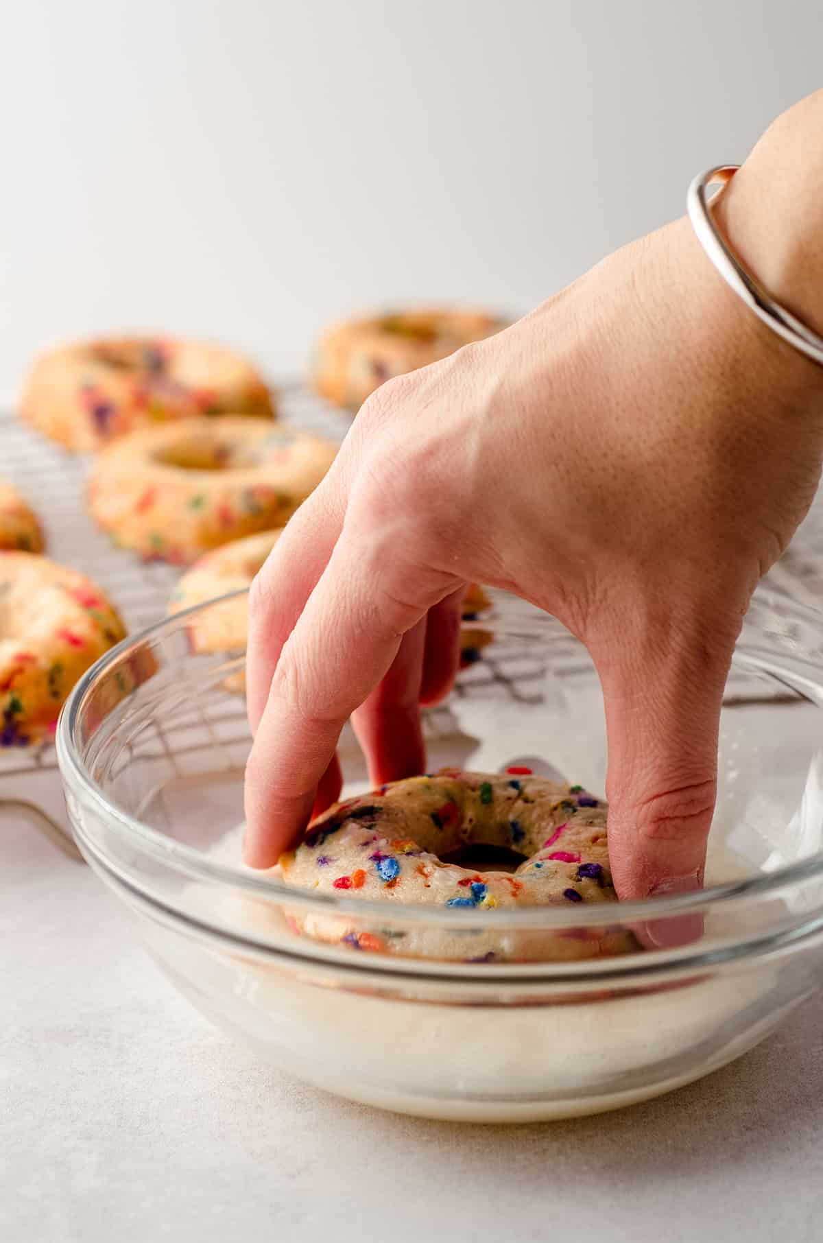 hand dipping a funfetti donut into glaze