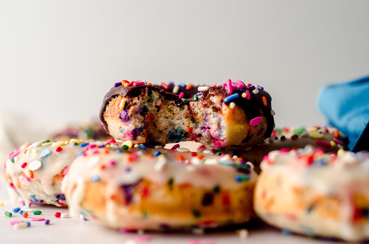 funfetti donuts in a stack and the one on top has a bite taken out of it