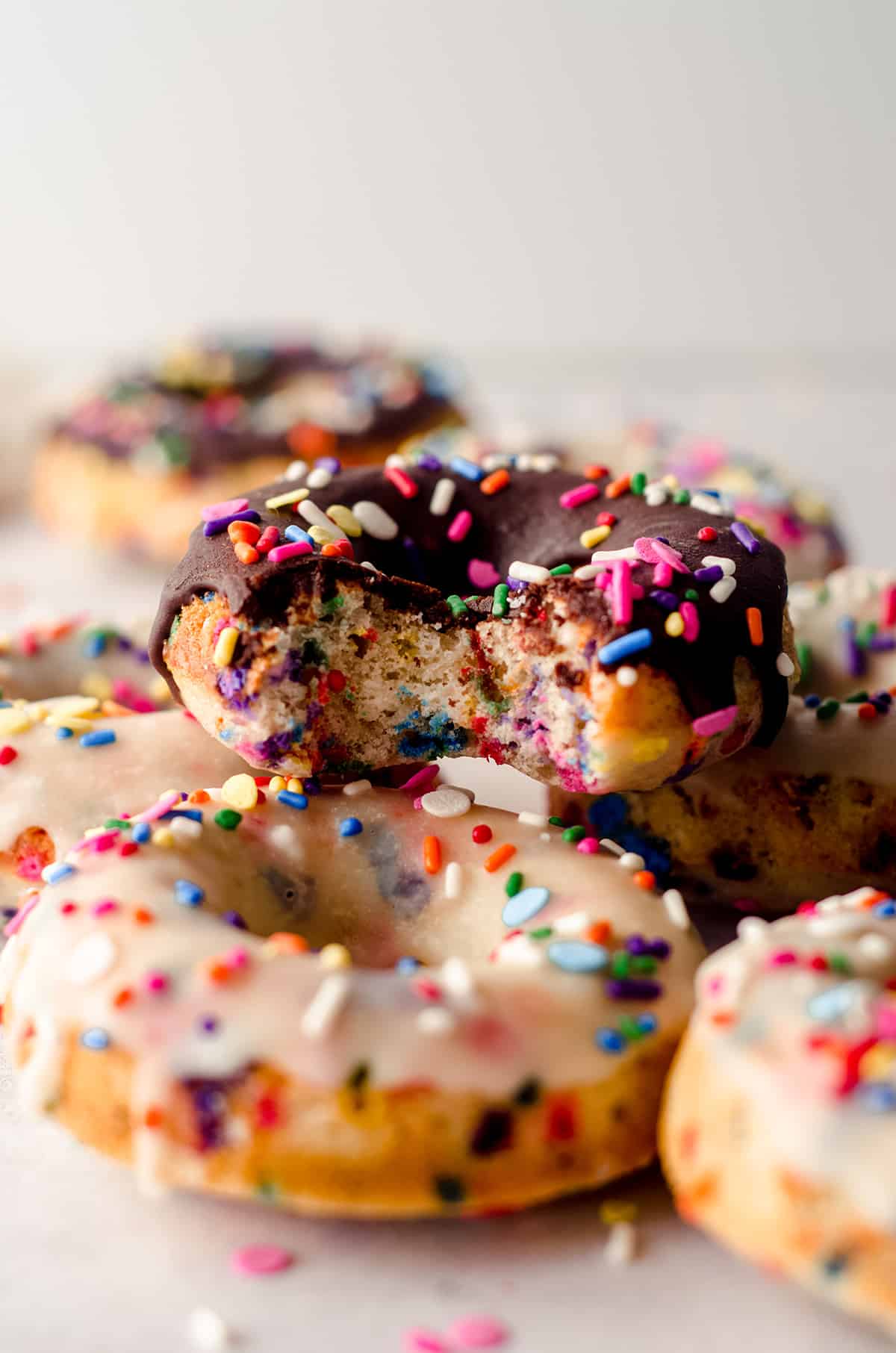 a stack of funfetti donuts and the one on the top has a bite taken out of it