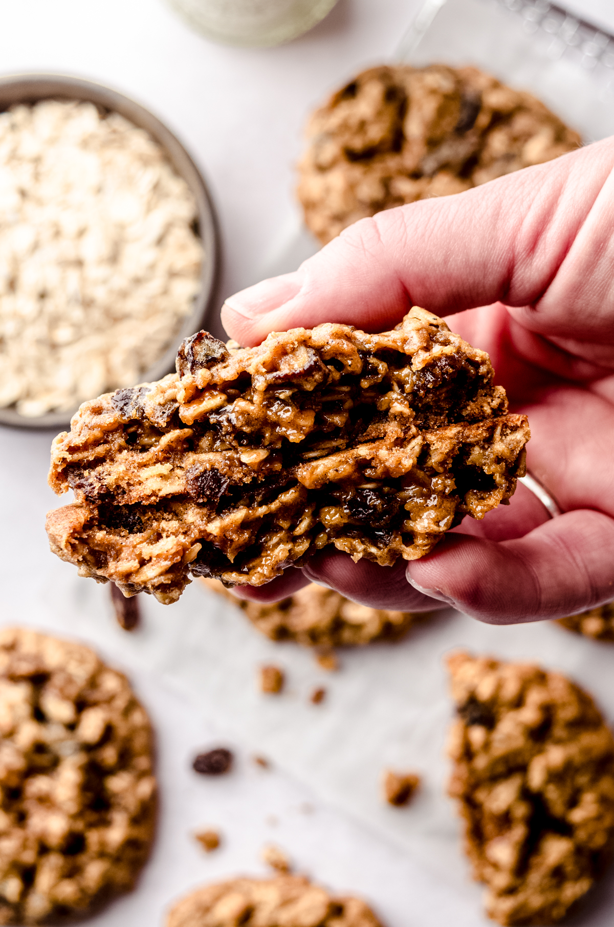 A hand holding a chewy oatmeal raisin cookie that has been broken in half so you can see the gooey inside.