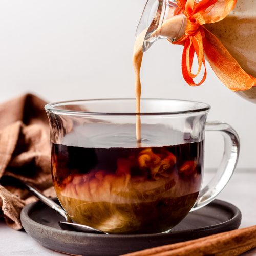 pouring pumpkin spice creamer into a cup of coffee