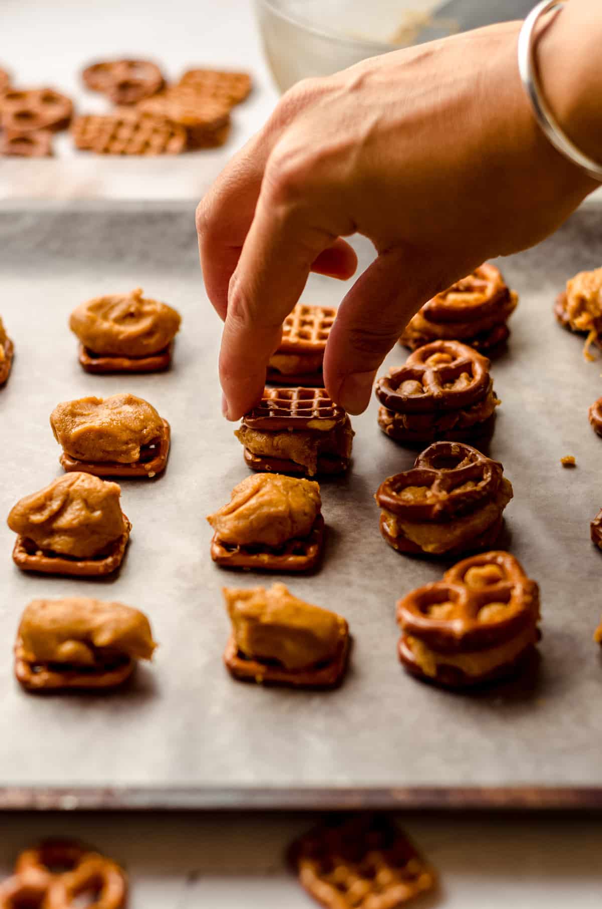 hand putting the pretzel tops on pumpkin peanut butter pretzel bites