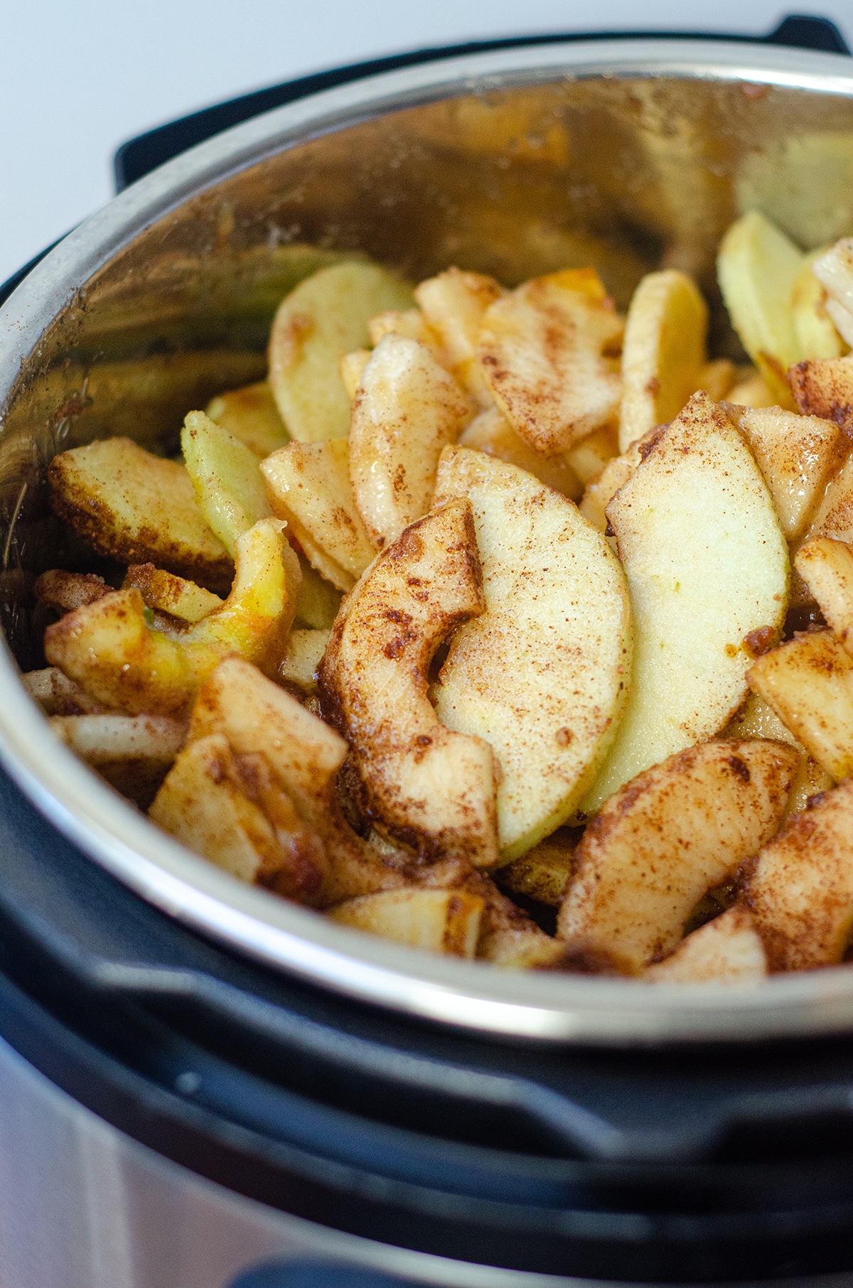 apples covered in sugar and spices in the bowl of an instant pot to make apple butter