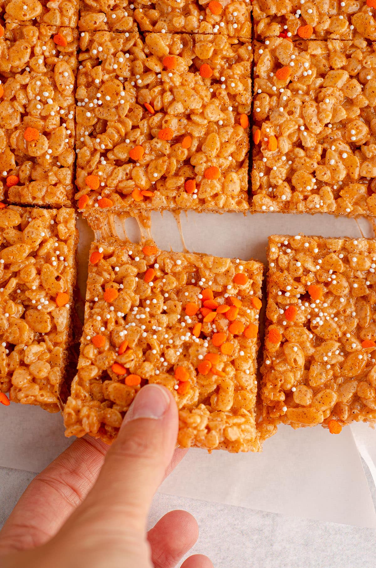 a hand pulling pumpkin rice krispies treats from a sliced batch