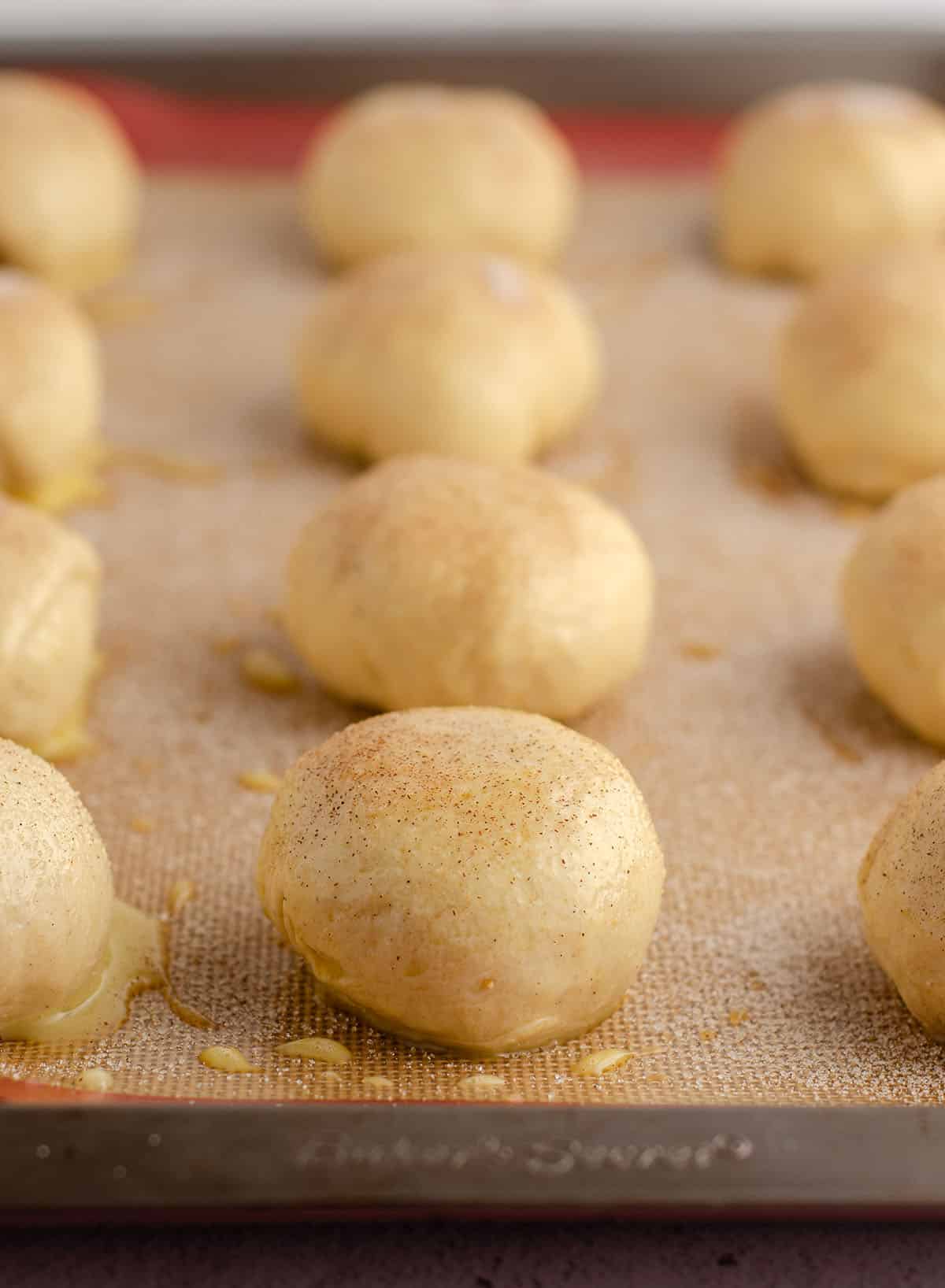 rolls brushed with an egg wash and sprinkled with cardamom-cinnamon-sugar on a baking sheet ready to bake