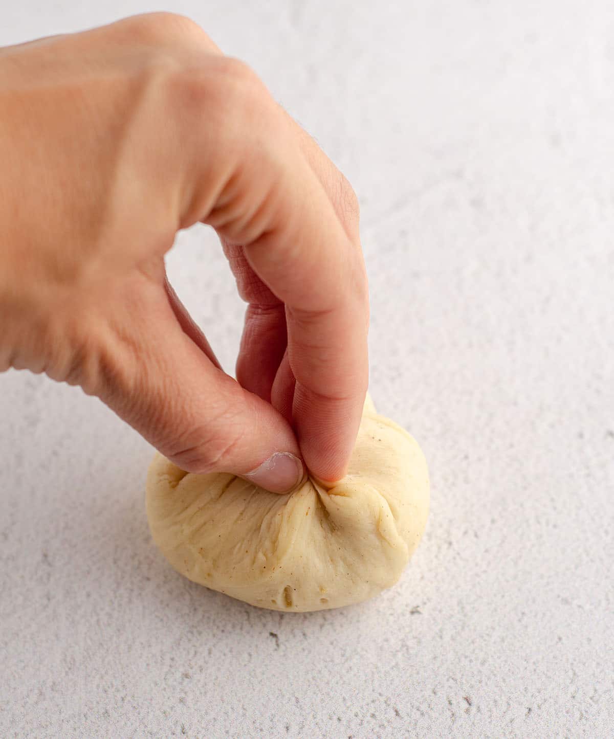 hands forming bread dough into a pouch for rolls