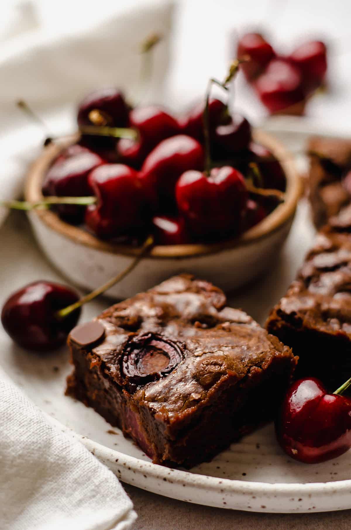 cherry brownies on a plate with a bowl of cherries