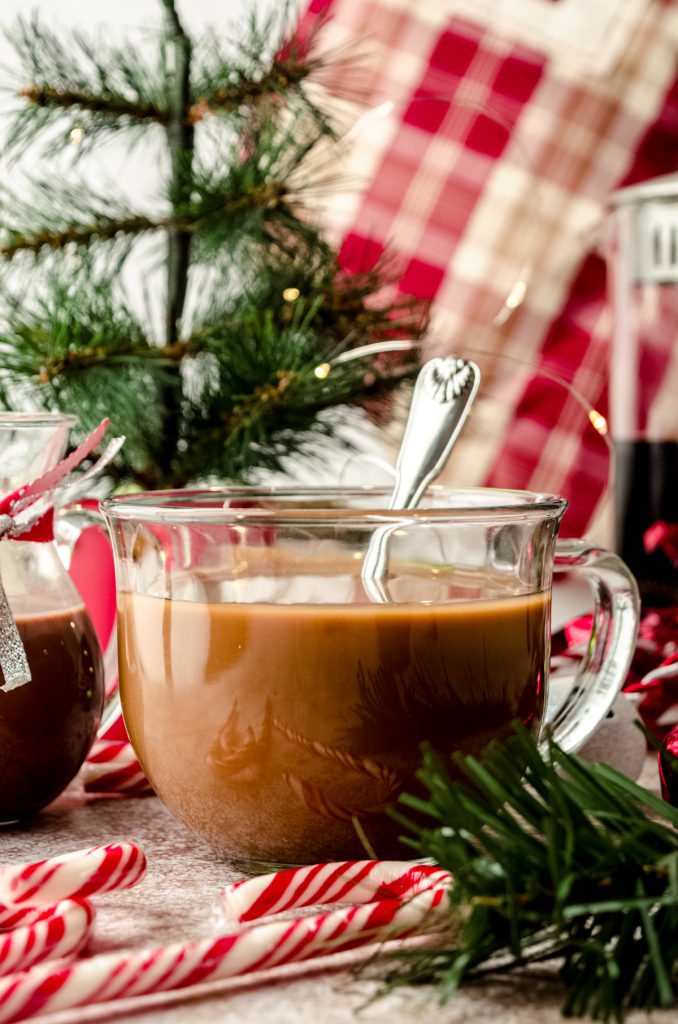 A cup of coffee with a spoon and peppermint mocha coffee creamer in it sitting in a Christmas scene.