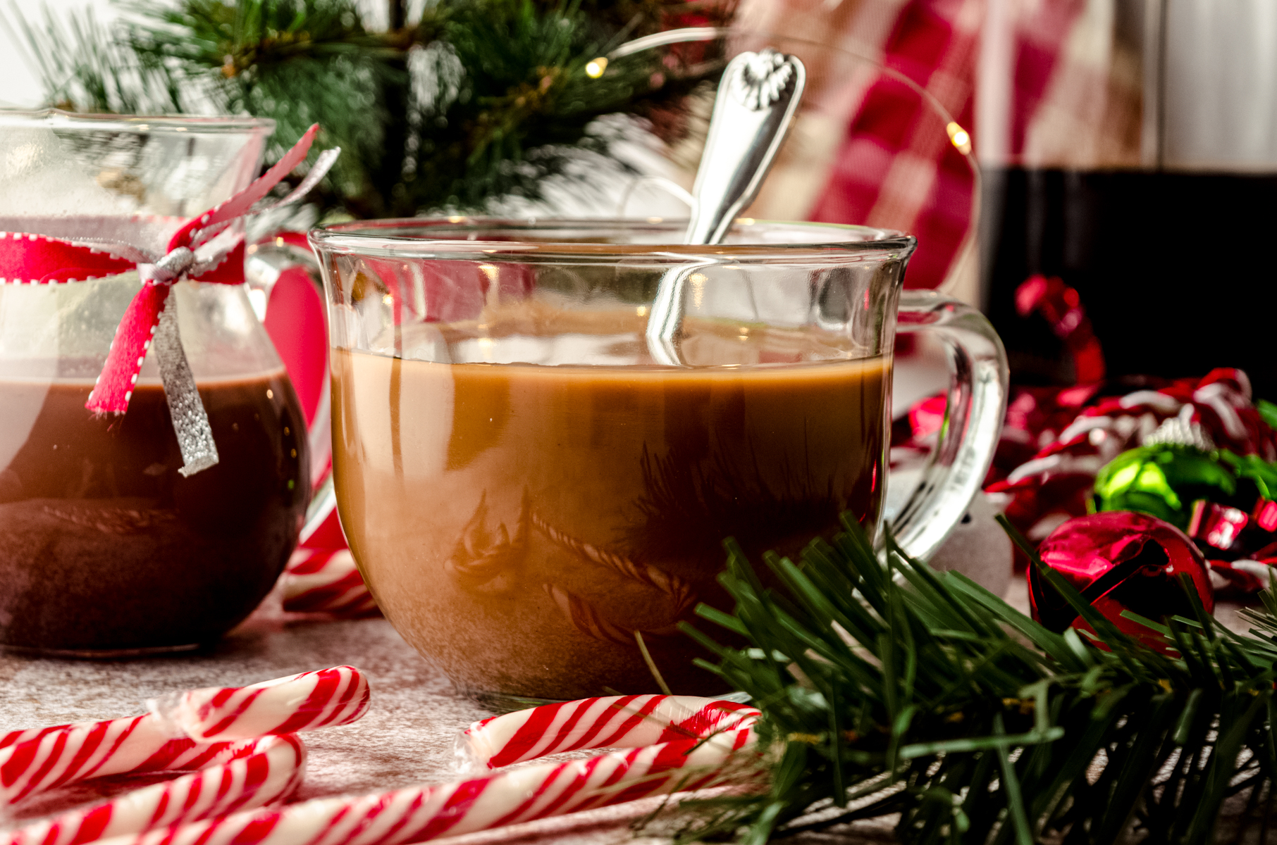 A cup of coffee with a spoon and peppermint mocha coffee creamer in it sitting in a Christmas scene.