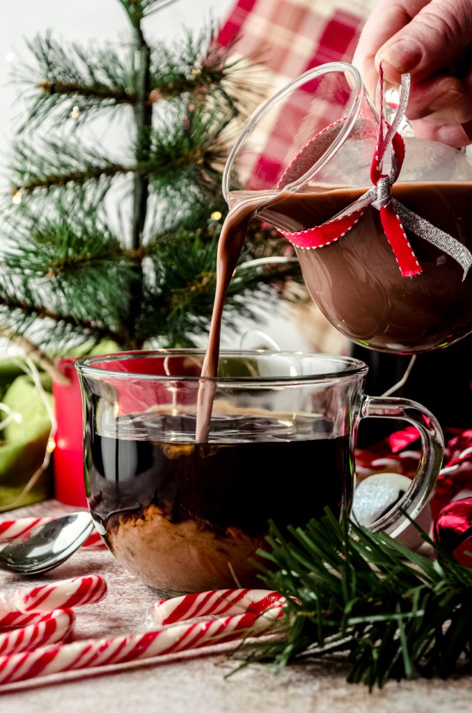 A photo of someone pouring peppermint mocha coffee creamer into a cup of coffee with Christmas decor in the back and foreground.