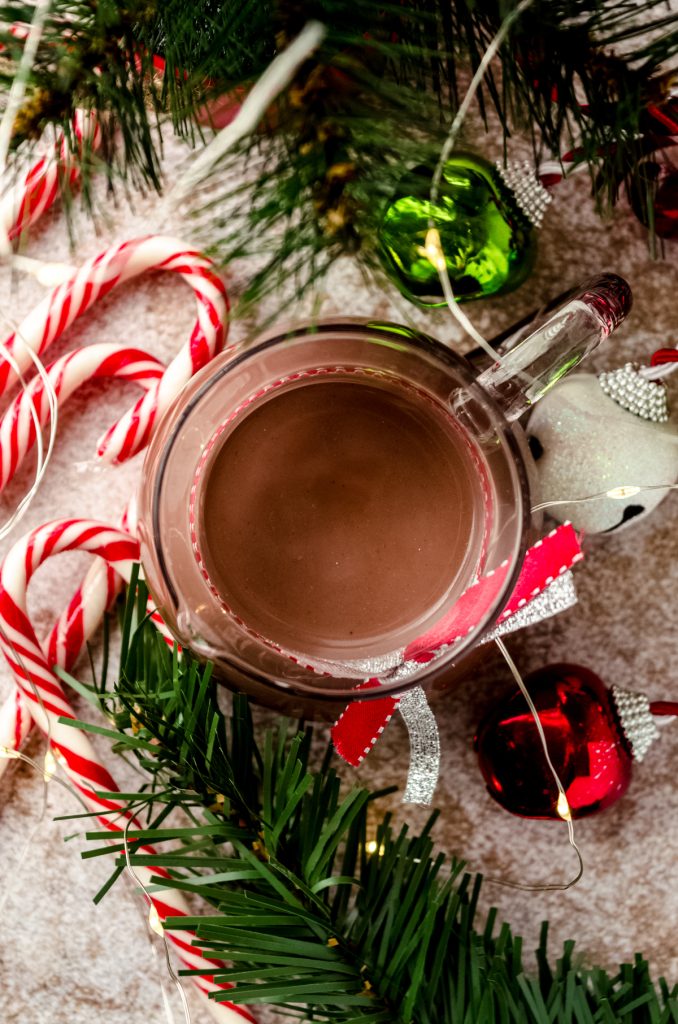 Aerial photo of a glass carafe of peppermint mocha coffee creamer with Christmas decor around it.