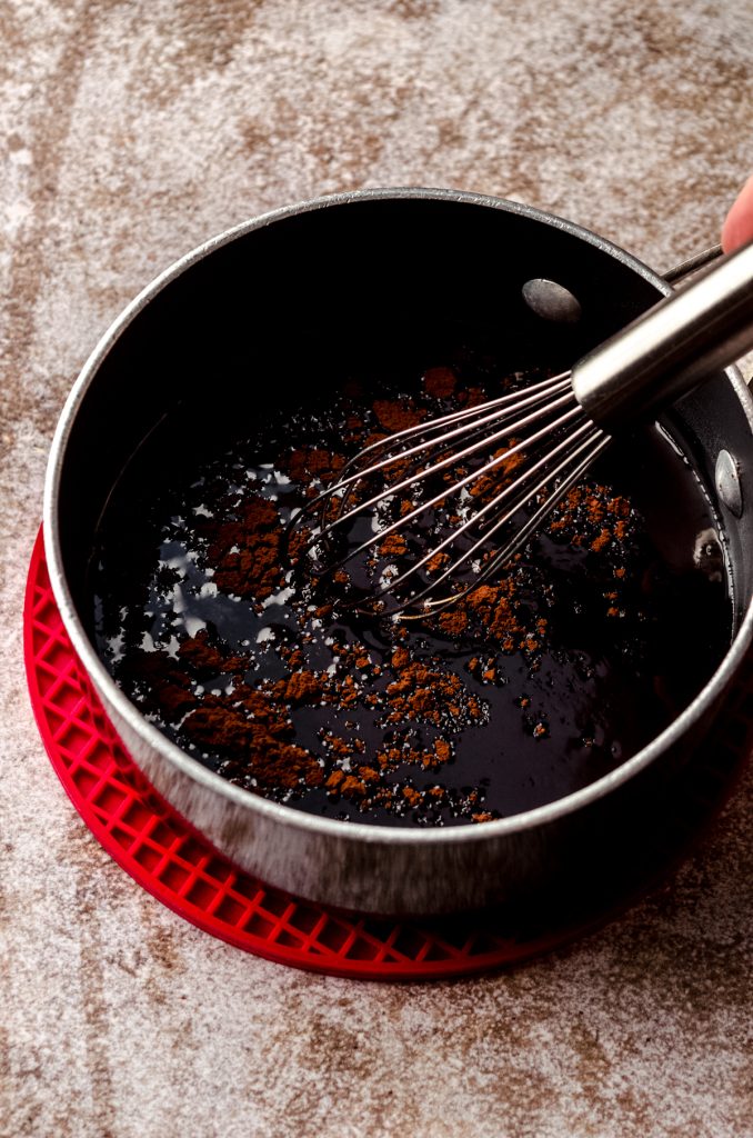 A saucepan of simple syrup with cocoa powder in it and a whisk.