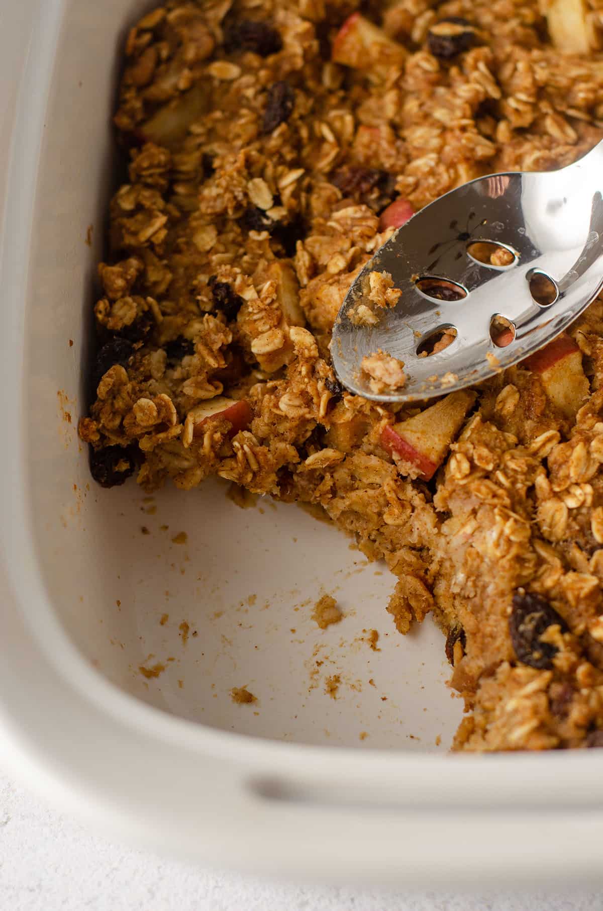 portion taken out of baked apple oatmeal in a casserole dish with a serving spoon