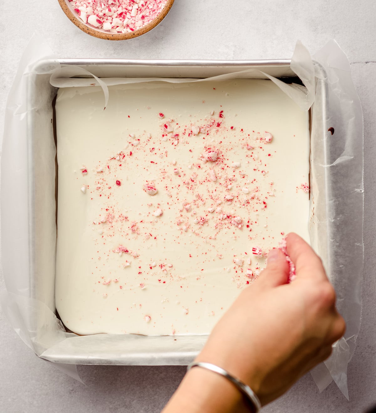 hand sprinkling crushed candy canes onto white chocolate to make peppermint bark