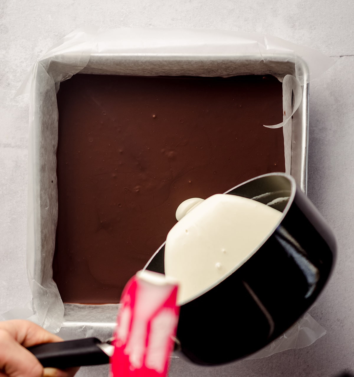 hand pouring white chocolate onto hardened semi-sweet chocolate layer to make peppermint bark
