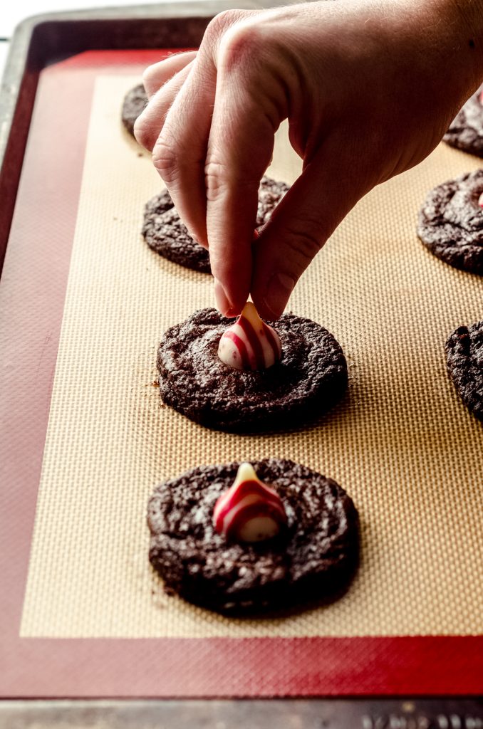 Someone is pressing a candy cane kiss into the top of a chocolate cookie to make a chocolate peppermint blossom.
