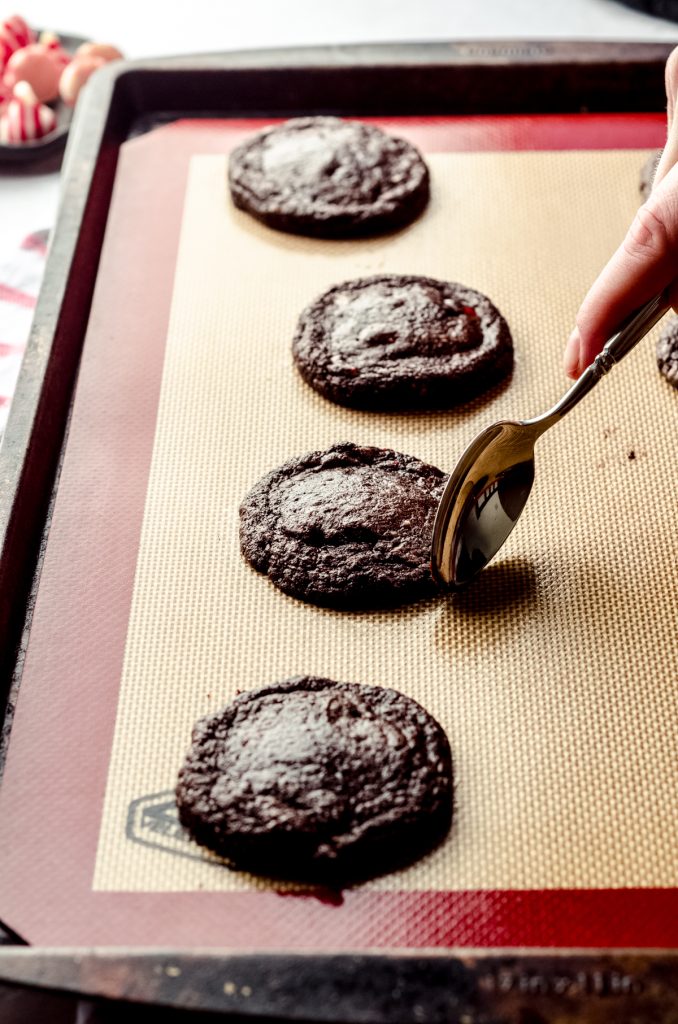 Someone is using a spoon to shape hot cookies straight out of the oven that are still on the baking sheet.